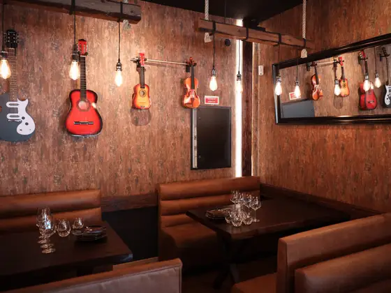 Bancos corridos em pele castanha sob guitarras e um violino pendurados na parede.