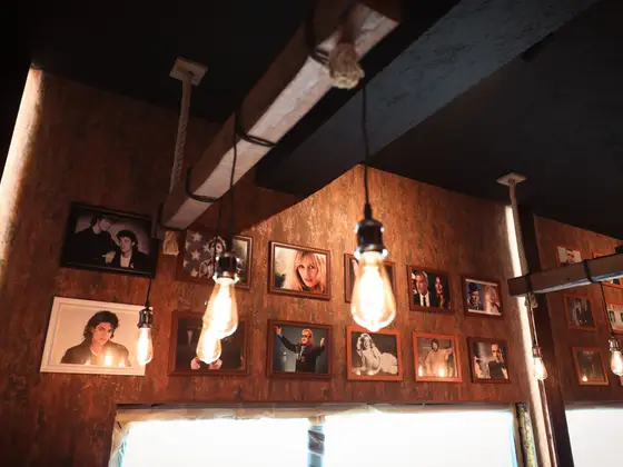 Parede de ferrugem com retratos emoldurados, entre lâmpadas de filamento.